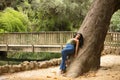 South American woman, young, beautiful, brunette, with colorful top and jeans leaning on the trunk of a big tree, relaxed and calm Royalty Free Stock Photo