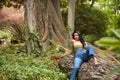 South American woman, young, beautiful, brunette, with colorful top and jeans sitting on a tree trunk, with sensual and Royalty Free Stock Photo