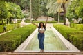 South American woman, young, beautiful, brunette, with crochet top and jeans standing next to a fountain, arms up, triumphant and