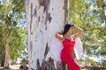 South American woman, young, beautiful, brunette with red dress and white wings, leaning on a tree trunk, pure, alone, relaxed and Royalty Free Stock Photo