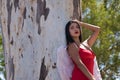 South American woman, young, beautiful, brunette with red dress and white wings, leaning on a tree trunk, in sensual and Royalty Free Stock Photo