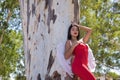 South American woman, young, beautiful, brunette with red dress and white wings, leaning on a tree trunk, in sensual and