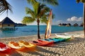 South Pacific beach scene with colorful kayaks on the sand and luxury resort bungalows over the water.