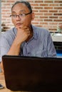 Southeast Asian Ethnicity mature adult man contemplating while working on a laptop at home. Thinking of continuation of his