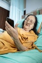 Southeast Asian female senior patient lying on hospital bed using smartphone Royalty Free Stock Photo