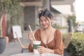 A Southeast Asian lady sitting outside the coffee shop puts the straw inside her coffee