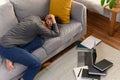 Southeast Asian male lying on the couch and holding his hand with notebooks and a computer nearby