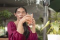 A Southeast Asian transwoman holds an iced juice and sits outside the cafe on a hot afternoon while staring at the side and Royalty Free Stock Photo