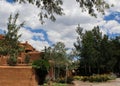Southwestern adobe architecture under a blue sky with fluffy white clouds and surrounded and framed by trees