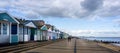 Southwold`s iconic beach huts and pier against a dramatic sky in Southwold, Suffolk, UK