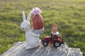 souvenir Easter bunny with painted red egg, toy model of tractor standing on tree bark in beautiful sunlight Royalty Free Stock Photo