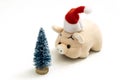 A souvenir pink pig or piggy bank in a red Santa Claus hat stands opposite a Christmas tree. Copy space. Shallow depth of field Royalty Free Stock Photo