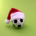 Souvenir soccer ball in a red Santa Claus hat on a green background. Copy space. The concept of sports Christmas gift. The symbol Royalty Free Stock Photo