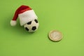 Souvenir soccer ball in a red Santa Claus hat next to a euro coin. green background. Christmas sporting events or New Year sports Royalty Free Stock Photo