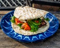 Souvlakia cooked at a campsite fire. Blue plate, red tomatoes, green vegetables, and pita bread