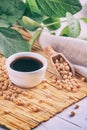 Soy sauce with soya beans scattered on a bamboo napkin against the background of burlap and branch young green pods soybean