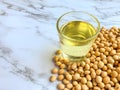 Soybean oil in a glass placed beside the soybean seed stack on a white marble background