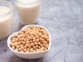 Soybeans in a heart-shaped bowl with soymilk in glass on grey concrete background.