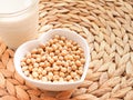 Soybeans in a heart-shaped bowl with soymilk in glass on rattan bamboo mat.