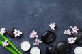 Spa background with massage pebble, green leaves, beautiful flowers and candles on black stone table top view. Aromatherapy.
