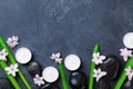 Spa background with massage pebble, green leaves, pink flowers and candles on black stone table top view. Aromatherapy and beauty