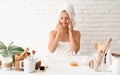 Happy young woman in white bathtowels applying creme on her face skin doing spa precedures Royalty Free Stock Photo