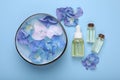 Spa composition. Aromatic water in bowl, flowers and bottles of essential oil on light blue background, flat lay Royalty Free Stock Photo