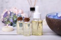 Spa composition. Bottles of essential oil and aromatic water with flowers in bowl on white wooden table, closeup