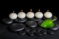 spa concept of row white candles and green leaf on black zen stones background with dew, closeup Royalty Free Stock Photo