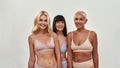Spa day. Three happy mature women in underwear smiling at camera while posing half naked in studio against light