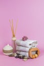 Spa essentials, aroma sticks stones, towels and a plant on a pink background