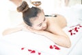 A spa masseuse is placing a hot stone on an Asian woman. Lying in a relaxing massage spa