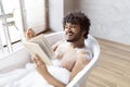 Spa procedure, self care and resting in bathroom. Happy young indian man in bath with foam, reading book in morning Royalty Free Stock Photo