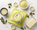 Spa products composition with sea salt, scrub, soap and bath towels on a white stone background with candles and green leaves.