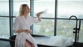 Spa relaxation. Young woman in spa bathrobe sitting at bath blowing foam in bathtub. Girl relaxing in bathroom at home