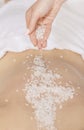 Spa scrub massage. Hands sprinkle salt on back of girl