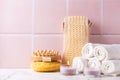 Spa setting with burning canles, towels, wisk, massager against pink tiled wall.