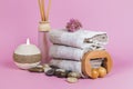 Spa essentials, aroma sticks stones, towels and a plant on a pink background