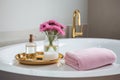 Spa setting with a white bathtub, a pink towel and a gold tray with skin care products