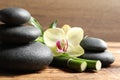 Spa stones, bamboo stems and beautiful orchid flower on wooden table, closeup Royalty Free Stock Photo