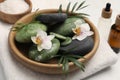 Spa stones, beautiful flowers and green leaves in wooden bowl on white marble table, closeup Royalty Free Stock Photo