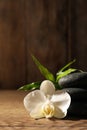 Spa stones, beautiful orchid flower and bamboo sprout on wooden table, closeup. Space for text Royalty Free Stock Photo