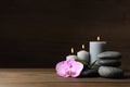 Spa stones, orchid flower, burning candles and bamboo sprout on wooden table. Space for text Royalty Free Stock Photo