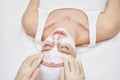In spa studio, young woman enjoys facial treatment. Beautician apply clay mask Royalty Free Stock Photo
