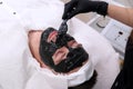 Spa therapy for men receiving facial black mask. Royalty Free Stock Photo