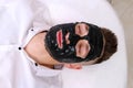 Spa therapy for men receiving facial black mask. Royalty Free Stock Photo