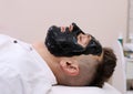 Spa therapy for men receiving facial black mask.