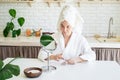 Happy young woman applying face scrub on her face in her home kitchen looking at the mirror Royalty Free Stock Photo