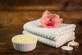 Spa or wellness set. Yellow sea salt in white bowl, towels, candle and pink flowers lily on brown wooden background. Selective Royalty Free Stock Photo