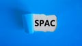 SPAC, special purpose acquisition company symbol. Words `SPAC` appearing behind torn blue paper. Beautiful blue background, copy